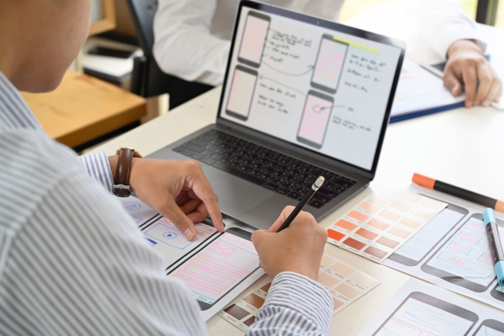 a man in front of a computer and papers sketching a user interface layout